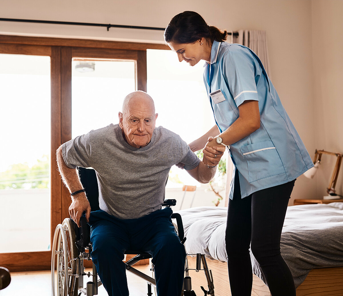 Senior wird aus Rollstuhl geholfen von Pflegerin.