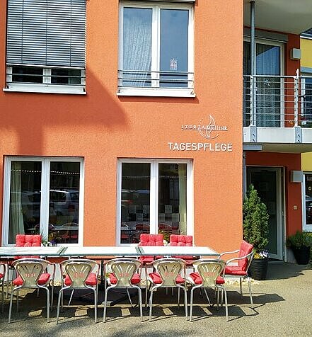 Ein Tisch mit Stühlen steht in der Sonne vor einem Haus mit der Aufschrift "Itertalklinik Tagespflege"