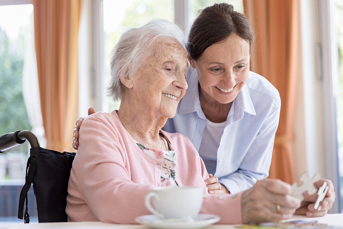 Seniorin und Pflegerin sind am puzzeln 